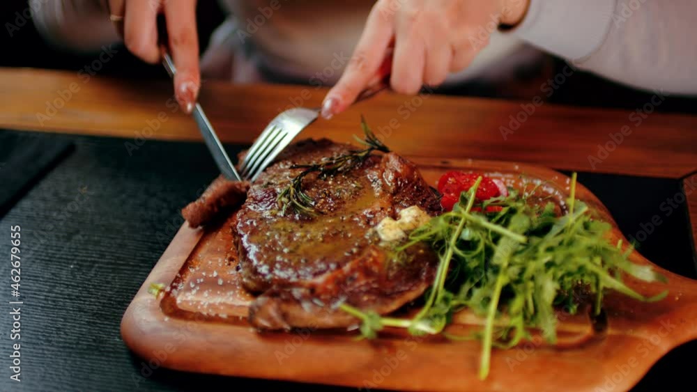 Succulent steak with vegetables on wooden board. Unrecognizable woman cuts off piece and eats. Food concept. Succulent steak with vegetables on wooden board. Unrecognizable woman cuts off piece and eats. Food concept.