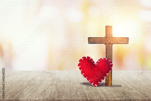 Red heart with a wooden Christian cross on floor in the morning light, photo