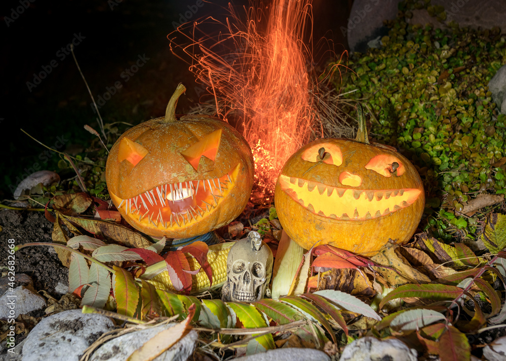carved pumpkins surrounded by sparks, smoke and fire, Halloween composition with smiling pumpkins and Halloween accessories, corn cobs, skull, Halloween party in autumn