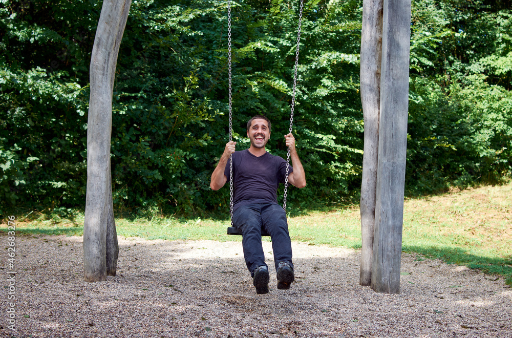 A young Hispanic man sitting on a swing in a park A young Hispanic man sitting on a swing in a park