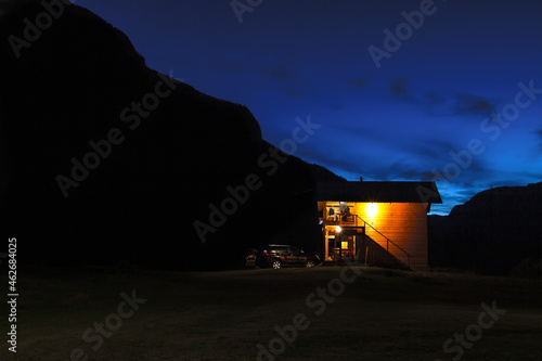 night view tourist base for recreation in the mountains. a car near a wooden house, people are sitting on the veranda are resting