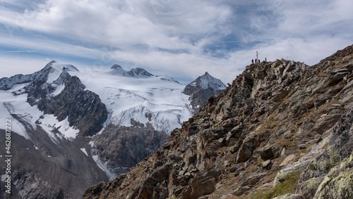 Hikers on the Grosser Trogler summit, Stubai high trail. View on the main Stubai mountain ridge with Wilder Freiger and Sulzenau glacier in Austrian Alps. Summit cross on the top of the mount. photo