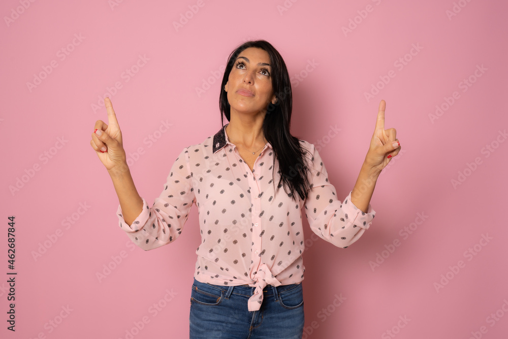 Smiling woman pointing fingers up over pink background Smiling woman pointing fingers up over pink background