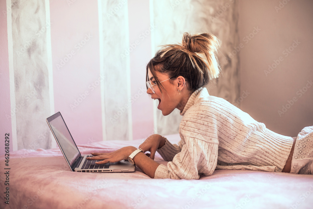 © Aitor Carrera Port√©/Westend61 - Surprised young woman lying on bed using laptop © Aitor Carrera Port√©/Westend61 - Surprised young woman lying on bed using laptop