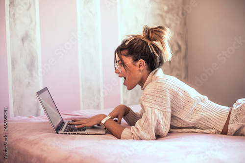 Surprised young woman lying on bed using laptop