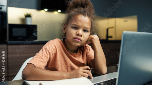Photos Sad biracial little girl looking at camera while doing homework at home