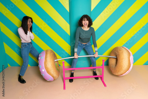 Two happy young women at an indoor theme park having fun with oversized donuts photo