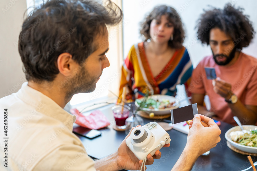 Friends having lunch in a restaurant looking at instant photos Friends having lunch in a restaurant looking at instant photos