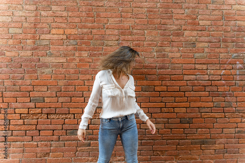 Portrait of youngwoman in front of a brick wall, shaking her head photo