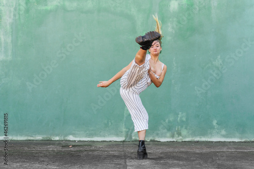 Young woman doing a high kick in front of green wall photo