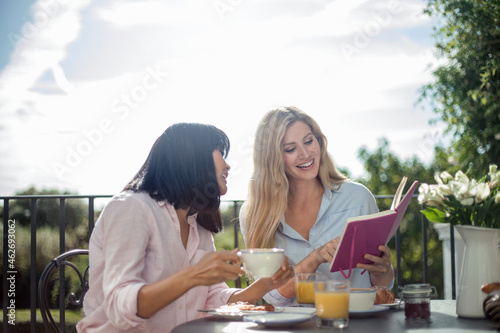 Two women having breakfast at outdoor cafe table  reading book