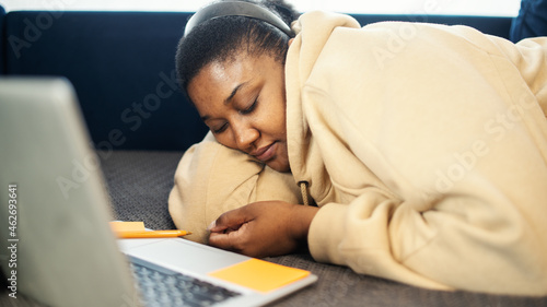 Billede på lærred Tired or bored  Black woman napping on sofa while working or having video call on laptop at home