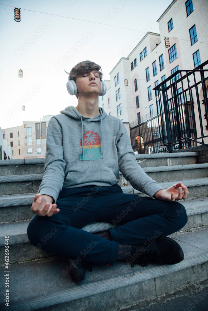 Teenager sitting on steps meditating in the city and listening to music