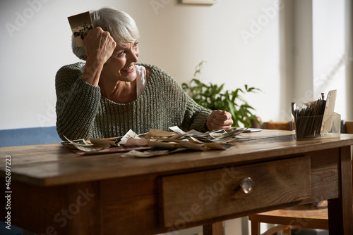 Happy senior woman sitting at table at home watching old photos photo