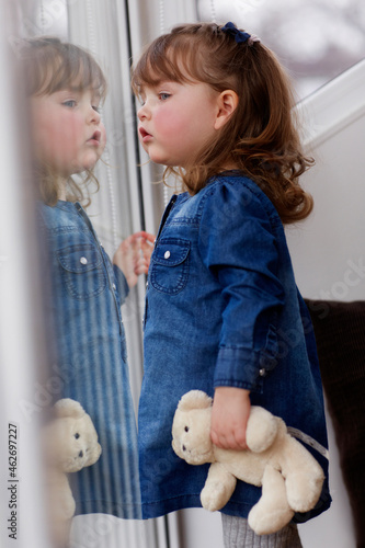 Portrait of curios toddler girl with teddy bear watching something