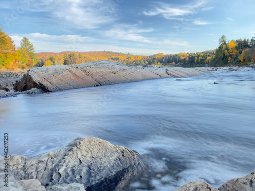 landscape of a bay and a waterfall in autumn  colorful mountains and trees  rocks among the water  blue sky  long exposure of the water current