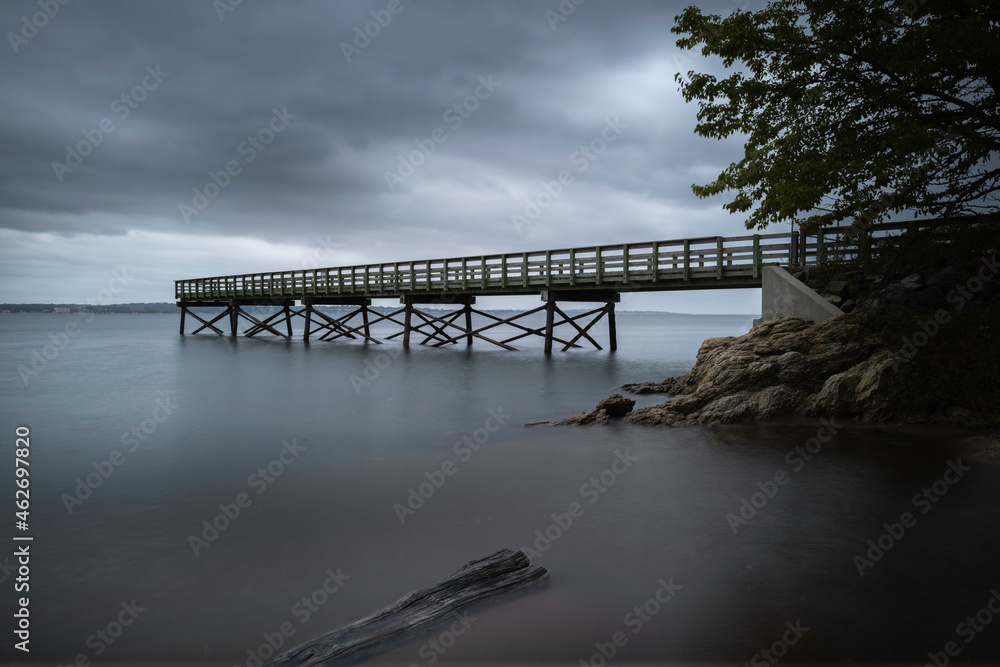 Pier, driftwood, rocks in the shore, long exposure photography. Moody weather and dramatic clouds in New Haven Harbor.