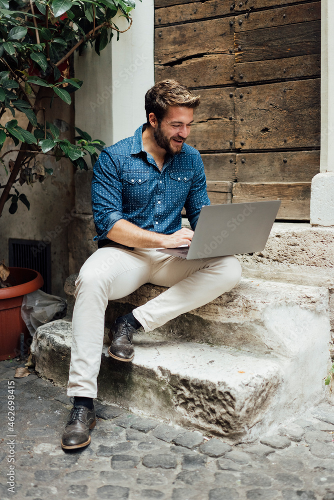 Laughing businessman sitting on steps in a courtyard using laptop Laughing businessman sitting on steps in a courtyard using laptop