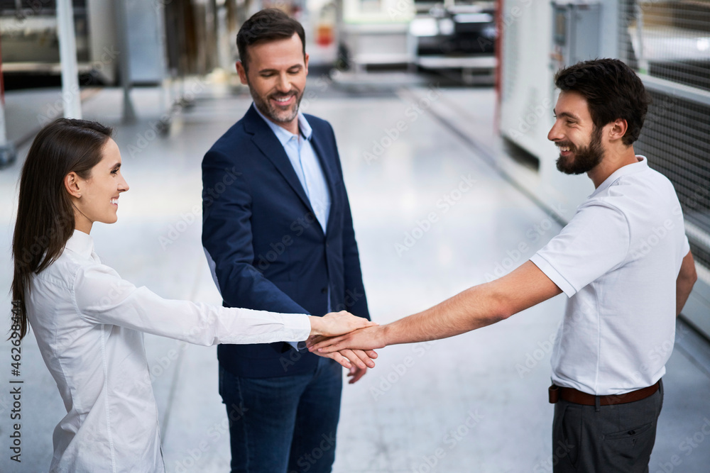 Businessman and employees stacking hands in a factory Businessman and employees stacking hands in a factory