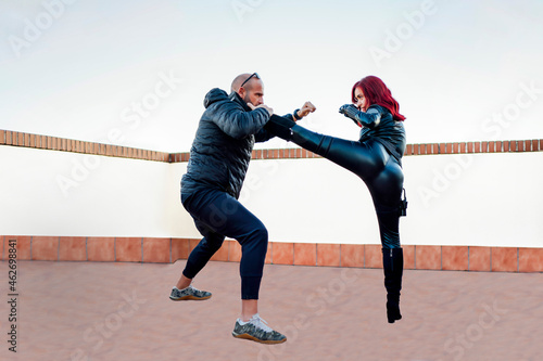 Redheaded woman wearing black leather catsuit fighting against man on rooftop photo