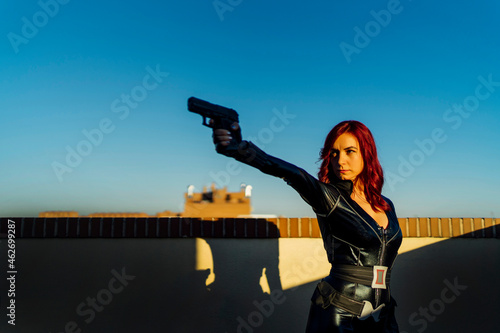 Portrait of redheaded woman with gun in her hand wearing black leather catsuit on rooftop photo