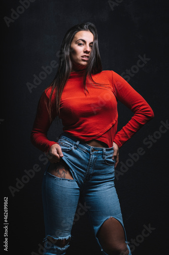 Portrait of young woman with tattoo on tigh posing in front of black background