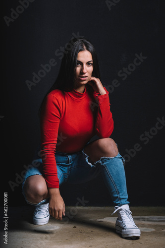 Portrait of young woman wearing bred shirt crouching in front of black background