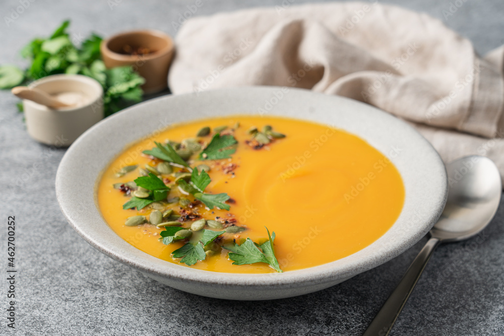Pumpkin puree cream soup with seeds, spices and green parsley leaves in gray terracotta plate on white plate. Autumn traditional food Pumpkin puree cream soup with seeds, spices and green parsley leaves in gray terracotta plate on white plate. Autumn traditional food