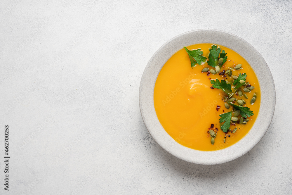 Pumpkin puree cream soup with seeds, spices and green parsley leaves in gray terracotta plate on white plate. Autumn traditional food Pumpkin puree cream soup with seeds, spices and green parsley leaves in gray terracotta plate on white plate. Autumn traditional food