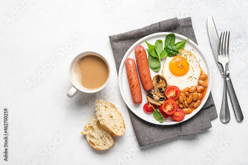 Traditional English breakfast with fried egg  beans in tomato sauce  grilled sausages  mushrooms and fresh tomatoes  served on plate. White background  flat lay