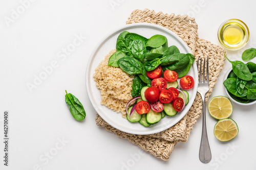 Fresh baby spinach, quinoa, tomato, cucumber salad on plate with white copy space. Vegan food balanced with plant protein and fresh vegetables