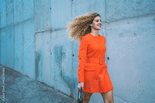 Happy young woman wearing red dress walking along street photo