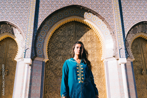 Young woman standing in front of traditional architure wearing Moroccan robe, Morocco photo