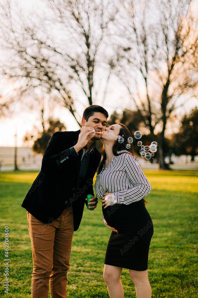 Expectant parents blowing soap bubbles in a park at sunset Expectant parents blowing soap bubbles in a park at sunset