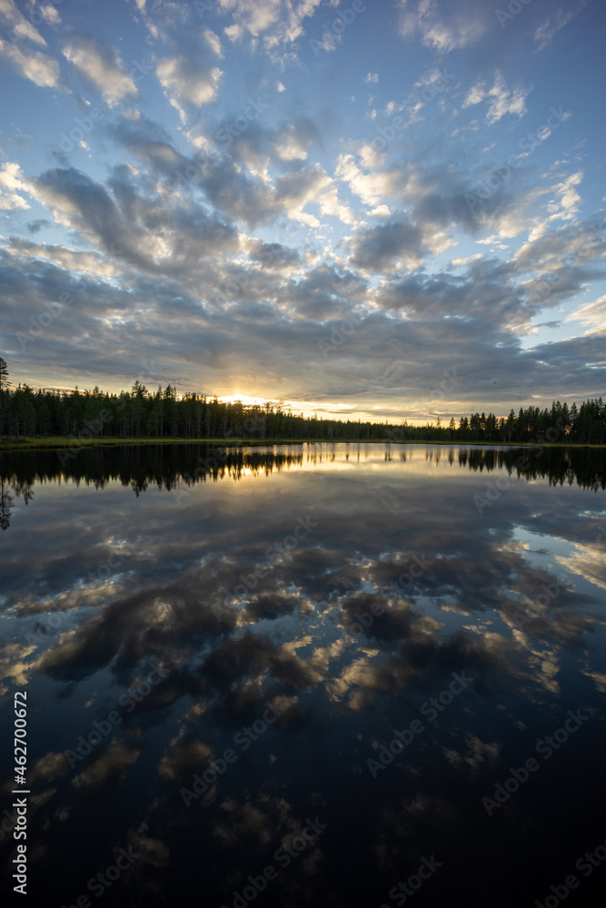 An epic lake view in Sweden near Glommersträsk. with open and cloudy sky and reflecting lake surface and a setting sun.