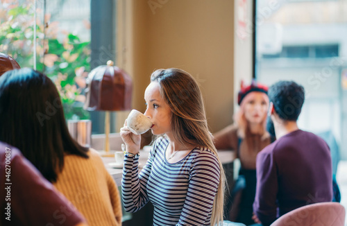 Young woman sitting in busy bar of a restaurant, drinking coffee photo