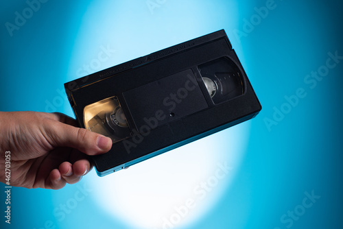 Hand holds retro HVS video cassette on a blue background. Retro wave. 80s 90s