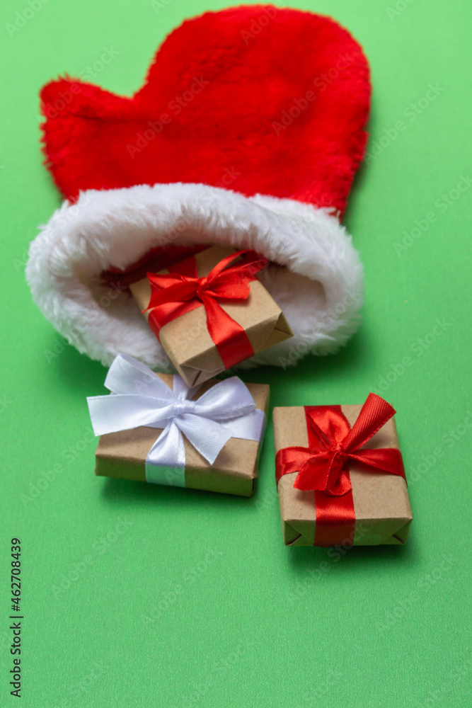 Christmas composition red mitten of santa claus with gifts on a green background. Template for postcards, packaging. Vertical photo