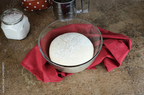 bread sourdough in a glass pan, yeast dough in a transparent bowl, wrapped in a burgundy cloth. top view. The process of cooking homemade cakes. Beige background. Kitchen utensils in the background.