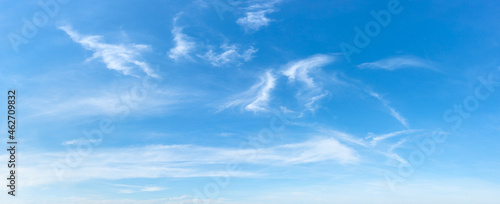 Clear azure sky with few wispy cirrus clouds. Sparse translucent white clouds in the blue sky on a sunny day. Concepts of weather forecast, vacations, travel and season. Sky only wide panorama. 