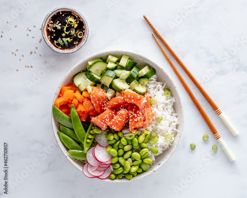 Salmon poke bowl with rice, edamame beans, cucumber, radish, mange tout, spring onion, bell peppers and a soy dipping sauce photo
