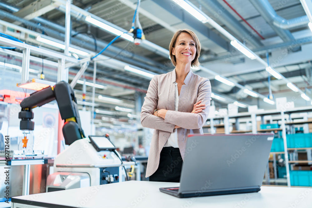 © Daniel Ingold/Westend61 - Smiling businesswoman with laptop in a modern factory hall
