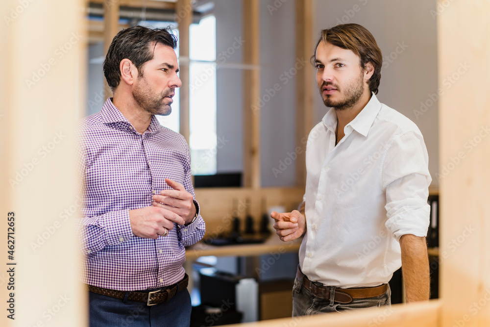 Two businessmen talking in wooden open-plan office Two businessmen talking in wooden open-plan office