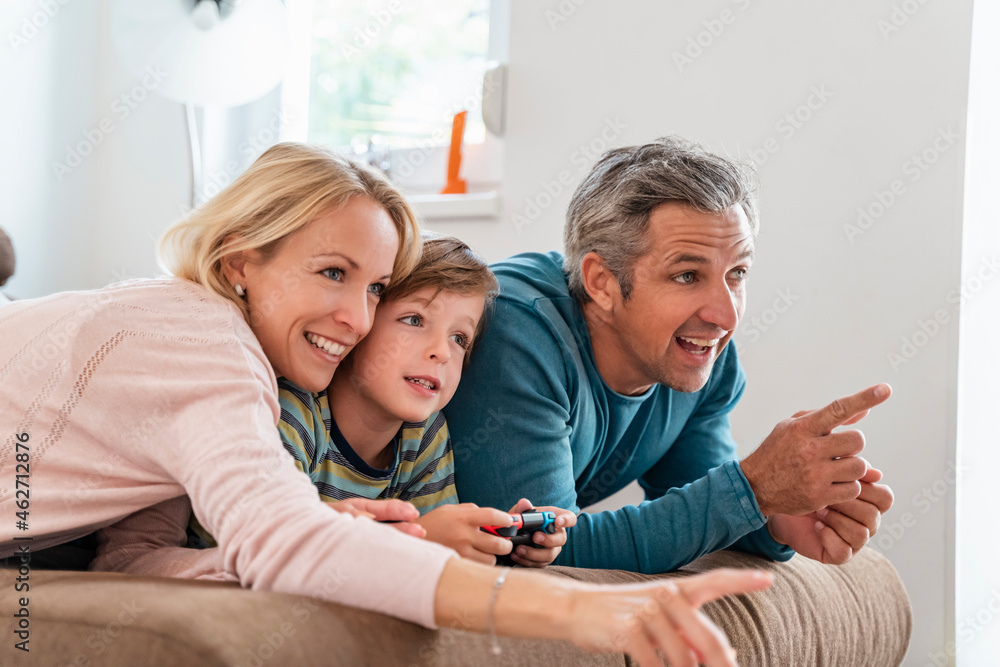Happy parents with son playing video game on couch at home Happy parents with son playing video game on couch at home