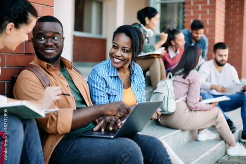 Group of happy university students talk and have fun while using laptop at campus.