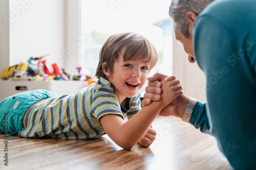 Father and son lying on the floor at home arm wrestling photo