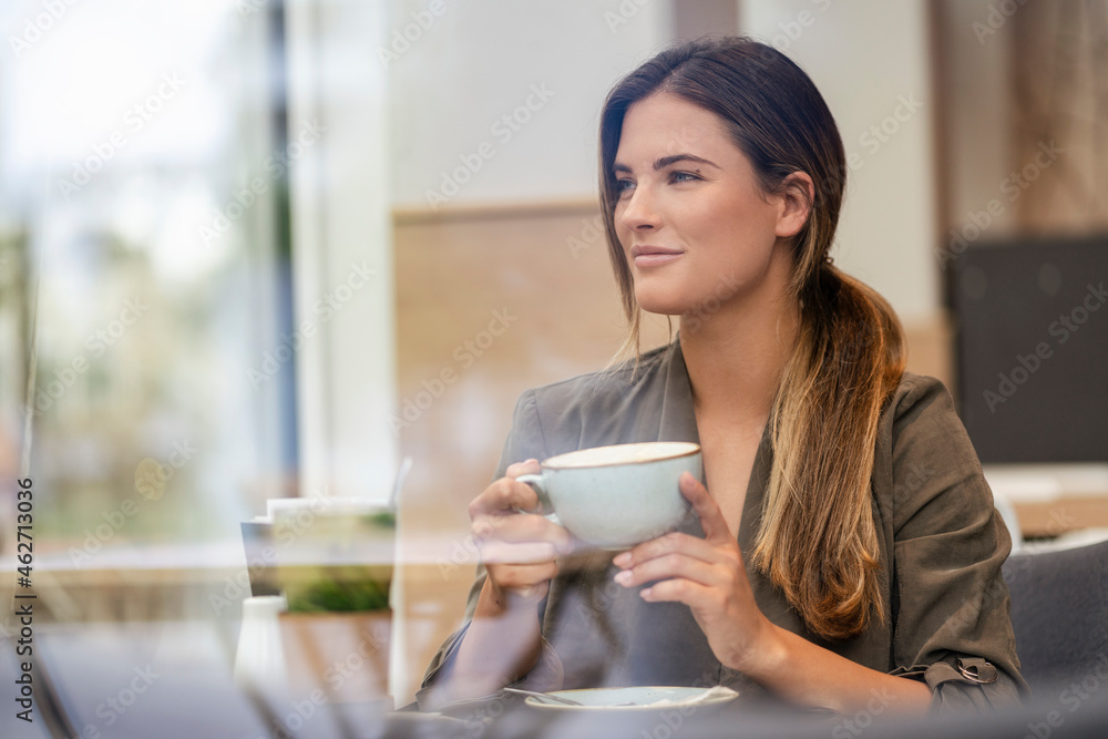 Young businesswoman with coffee cup in a cafe, seen through window Young businesswoman with coffee cup in a cafe, seen through window