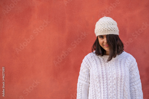 Portrait of smiling teenage girl in fornt of red wall wearing white knitwear photo