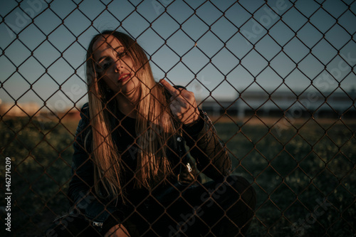 Portrait of young woman sitting behind wire mesh fence giving the finger photo