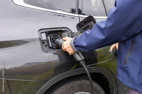 Close up view of man connecting charging cable to charging station for electric car. Sweden. 